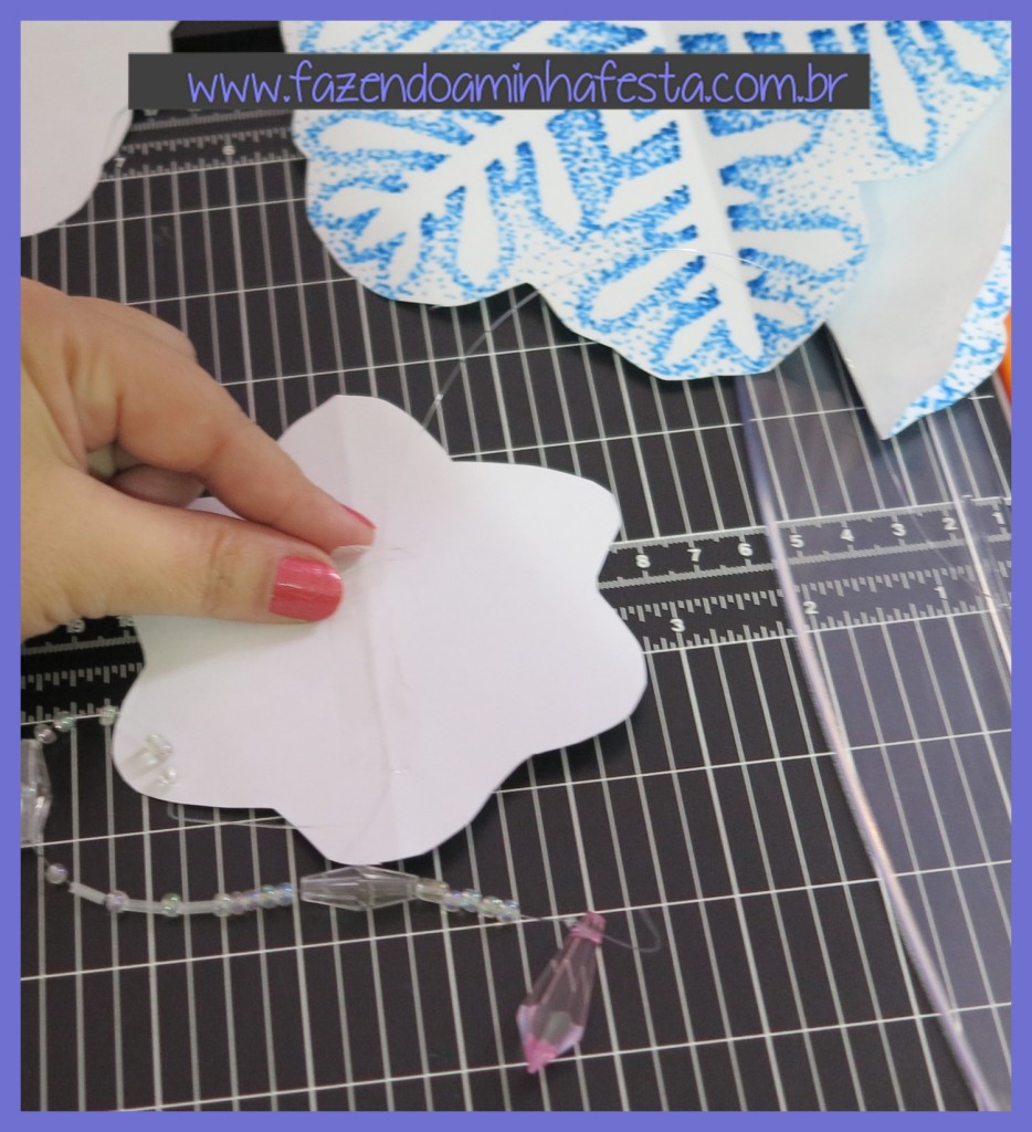 Pegue um dos moldes pequeno, e cole um fio de nylon com fita adesiva bem no meio. Deixe um pedaço grande do fio para um dos lados. Do outro lado você pode fazer uma decoração com cristais e miçangas.